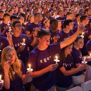 一大群学生——都穿着紫色的Go Frogs t恤，每个人都拿着点燃的蜡烛——聚集在校长大会上